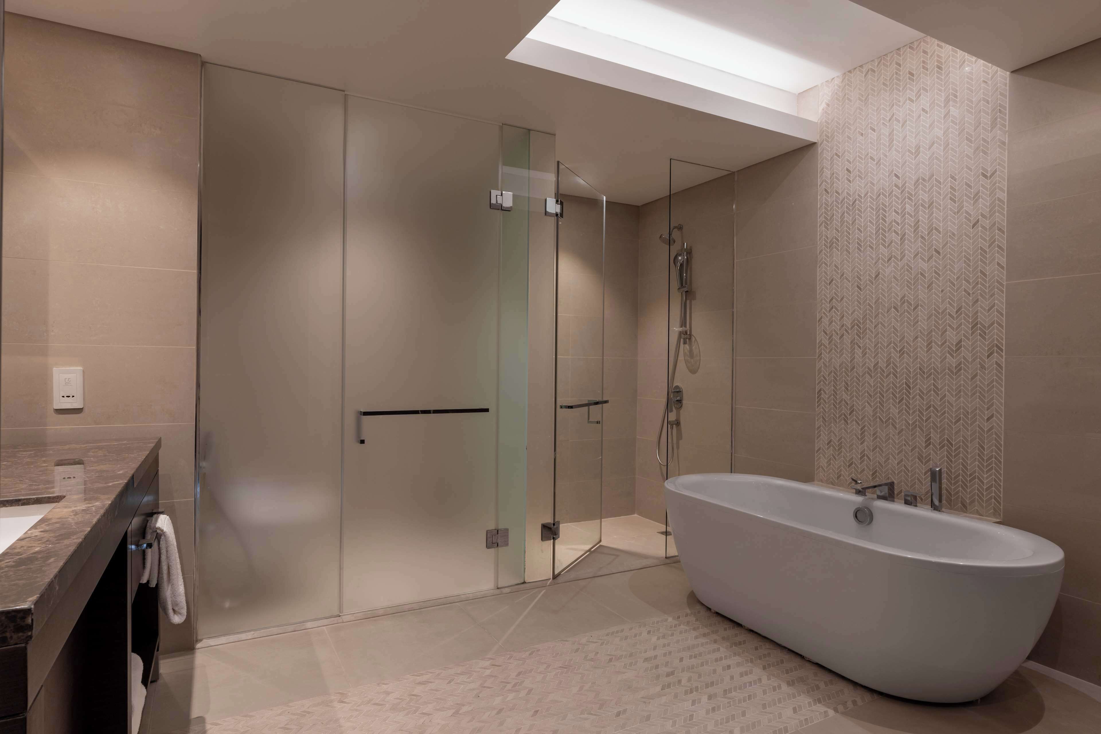 Un baño moderno con una bañera independiente, ducha con mampara de vidrio y encimera de mármol.