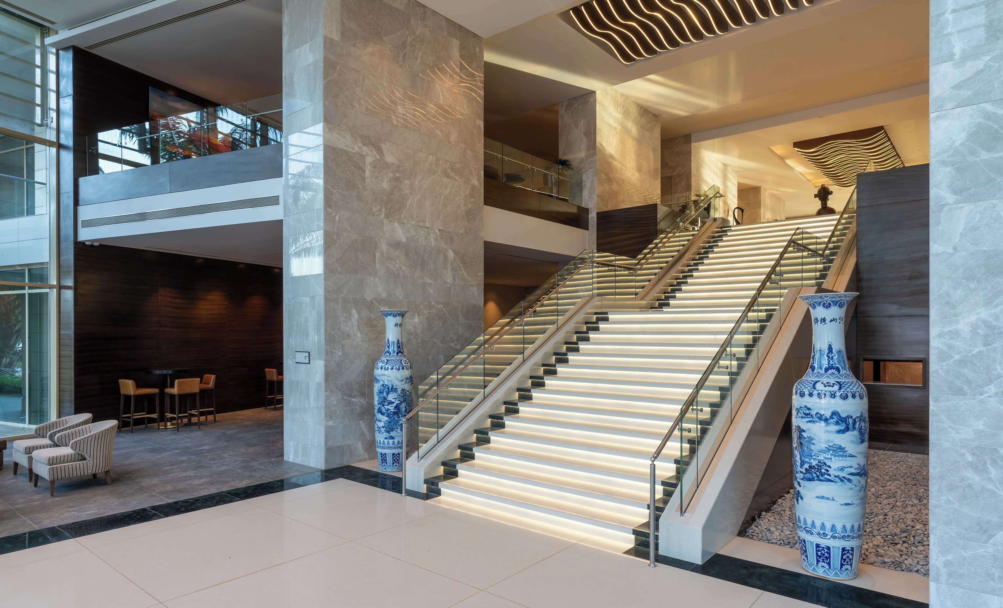 A modern hotel lobby with a grand staircase, seating area, and decorative vases.