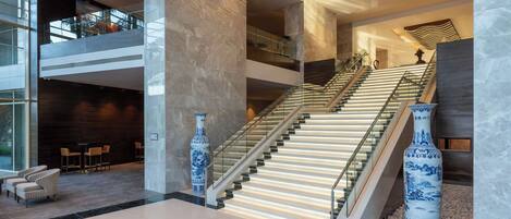 A modern hotel lobby with a grand staircase, seating area, and decorative vases.