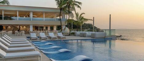 A pool area with lounge chairs, a glass-enclosed building, and palm trees.