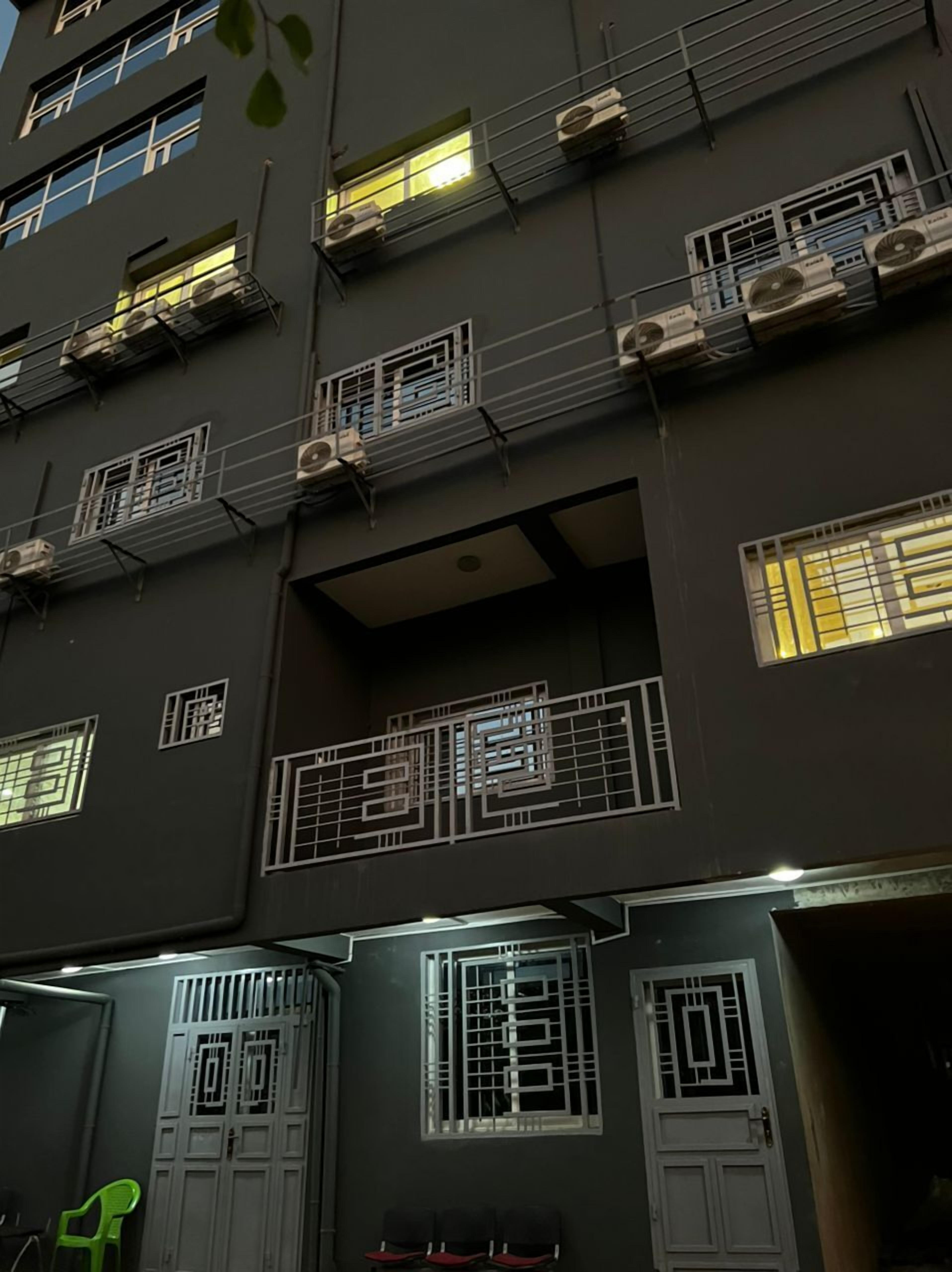 Un edificio de varios pisos con unidades de aire acondicionado, ventanas protegidas por rejas y una puerta con portón metálico.