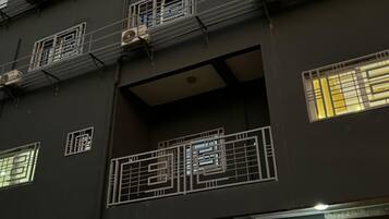 Un edificio de varios pisos con unidades de aire acondicionado, ventanas protegidas por rejas y una puerta con portón metálico.