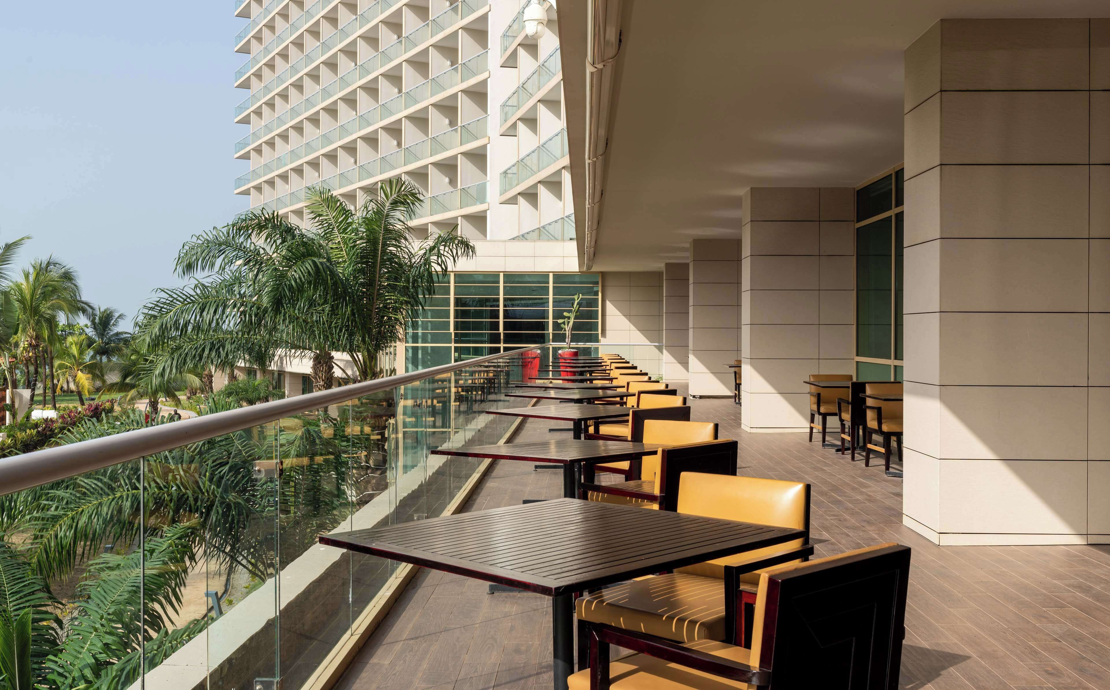 Un espace extérieur moderne aménagé avec des tables et des chaises, offrant une vue sur un jardin luxuriant et un immeuble de grande hauteur.