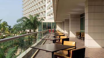 Un espace extérieur moderne aménagé avec des tables et des chaises, offrant une vue sur un jardin luxuriant et un immeuble de grande hauteur.