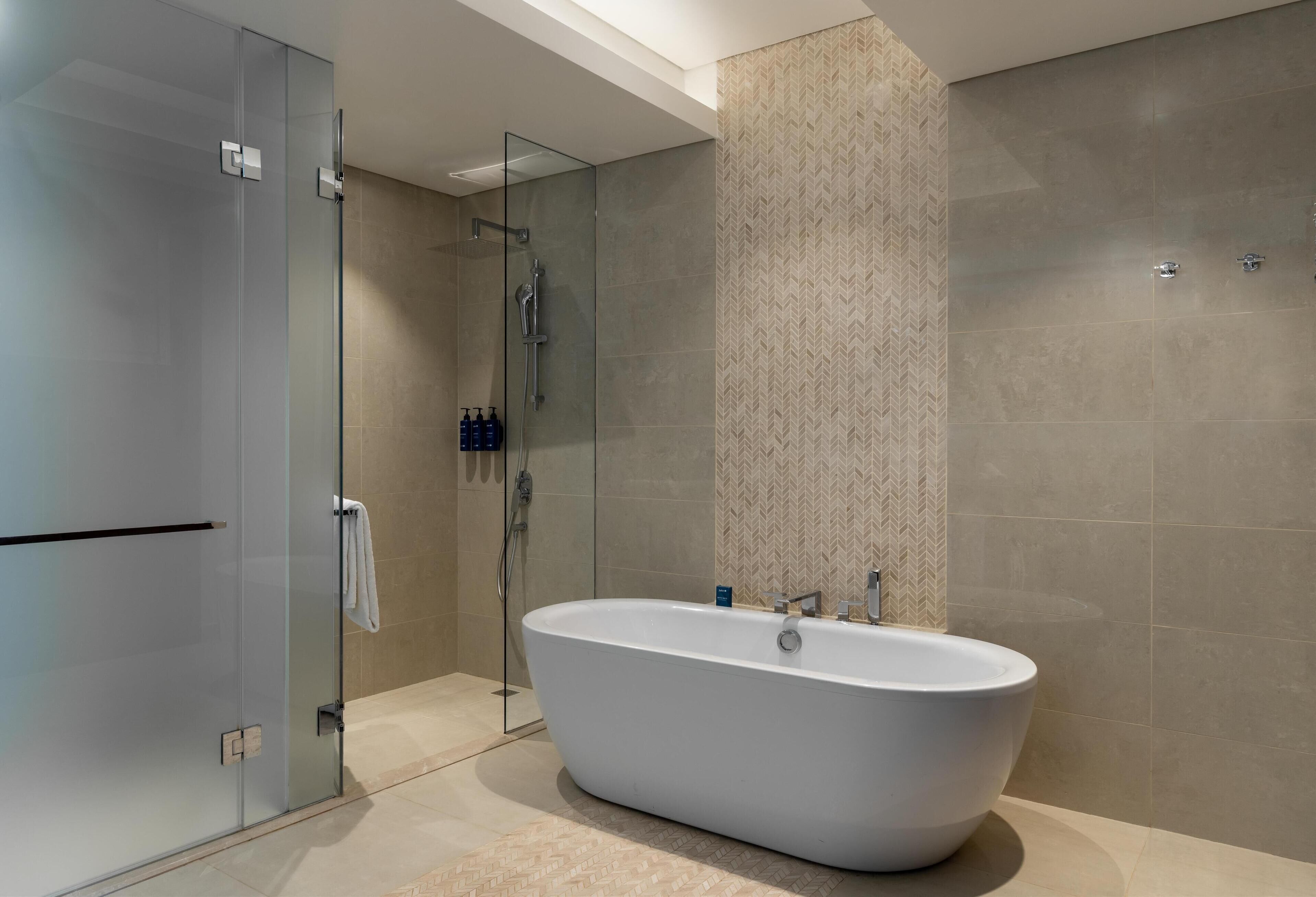 A modern bathroom with a freestanding bathtub, glass shower enclosure, and patterned wall tiles.