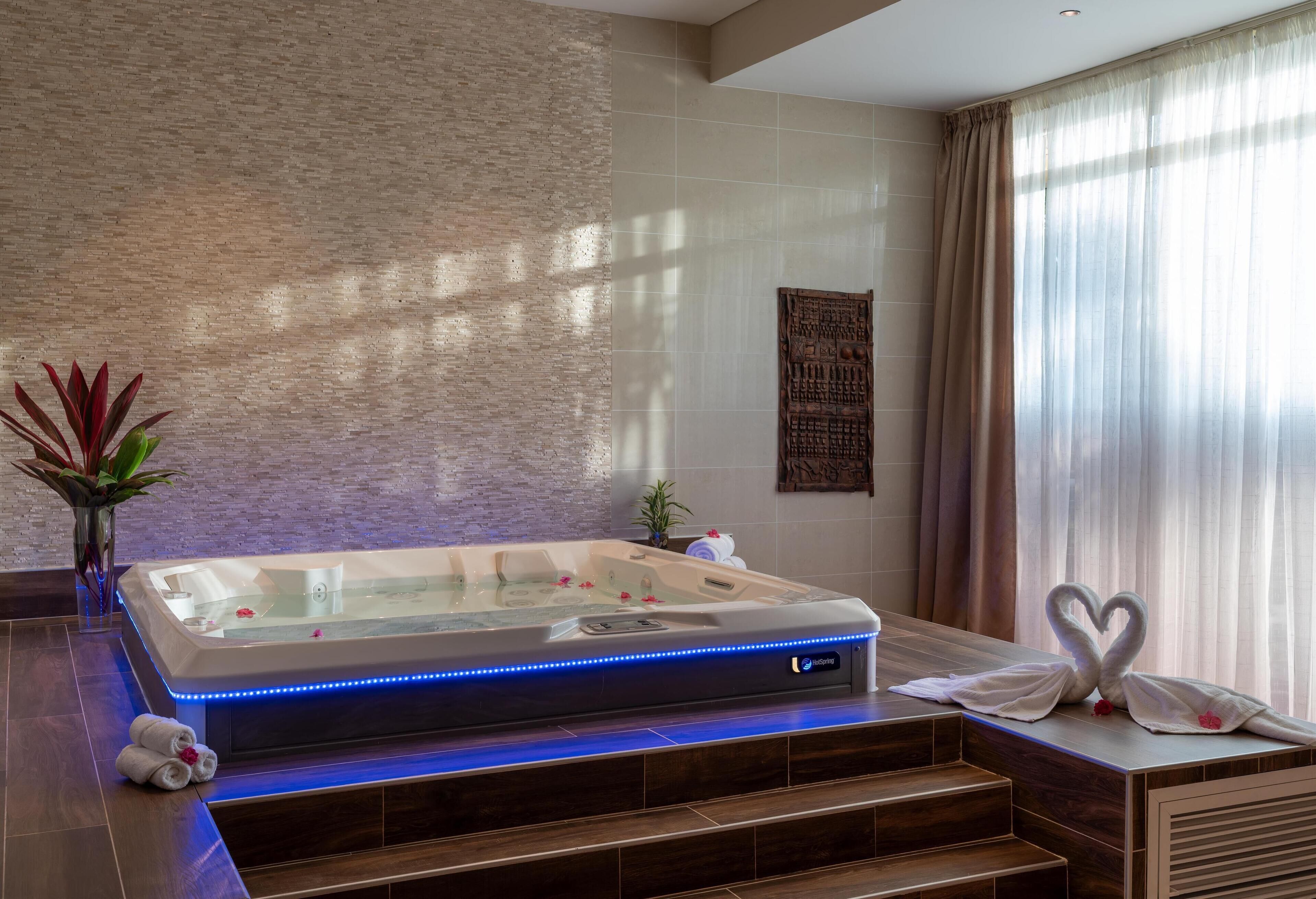 A spa room with a hot tub, wooden steps, and a wall-mounted artwork.