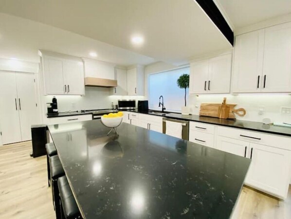 A modern kitchen with white cabinets, a black countertop, and a central island with a bowl of lemons.