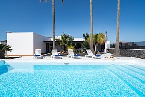 A pool area with lounge chairs, palm trees, and a modern building with a white facade.