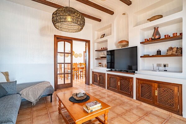 A living room with a sofa, a wooden coffee table, a TV, and shelves with decorative items.