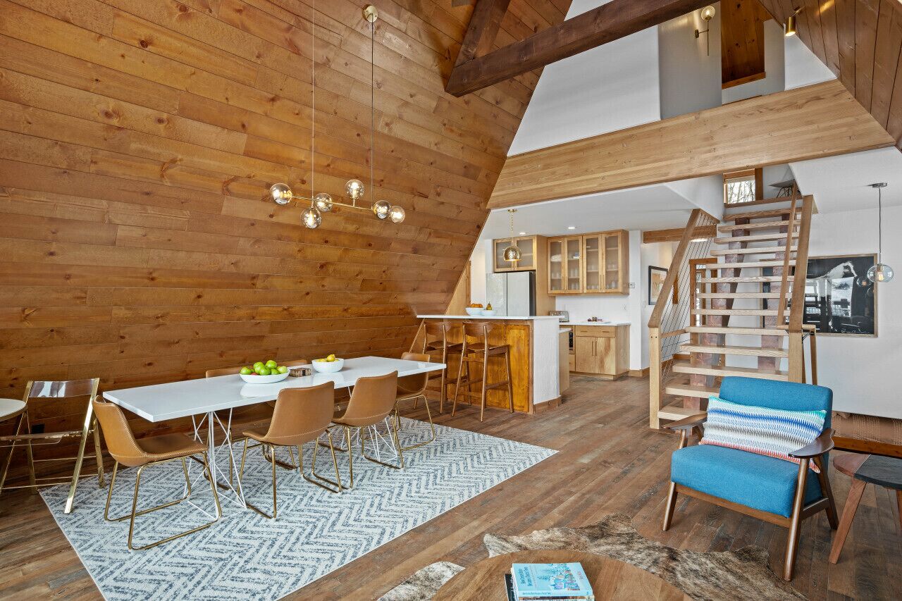 Een ruime loft met een hoge plafond, houten balken, een eethoek met een witte tafel en stoelen, een keuken met houten kasten, en een trap.