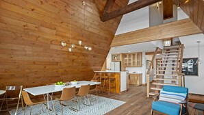 A spacious loft with a high ceiling, wooden beams, a dining area with a white table and chairs, a kitchen with wooden cabinets, and a staircase. - Mid-Century Mountain Home, Fully Remodeled, Style & Comfort in Crested Butte, CO (Crested Butte)