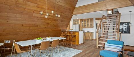 Een ruime loft met een hoge plafond, houten balken, een eethoek met een witte tafel en stoelen, een keuken met houten kasten, en een trap.