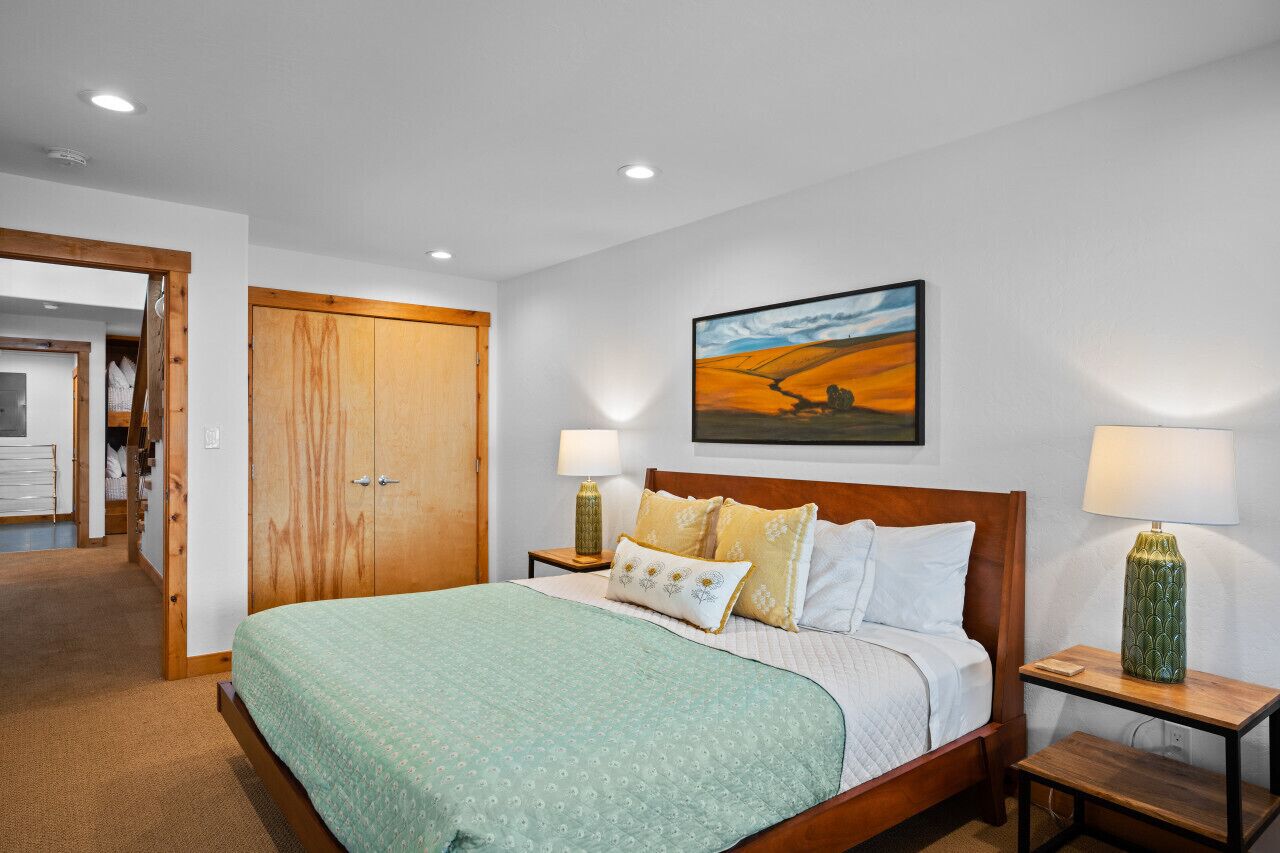 Een slaapkamer met een bed, twee nachtkastjes met lampen, een houten garderobe, een schilderij aan de muur en een vloerbedekking.