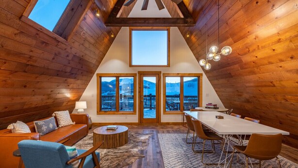 A cozy room with wooden walls, a large skylight, a sofa, a dining table, and chairs. - Mid-Century Mountain Home, Fully Remodeled, Style & Comfort in Crested Butte, CO (Crested Butte)