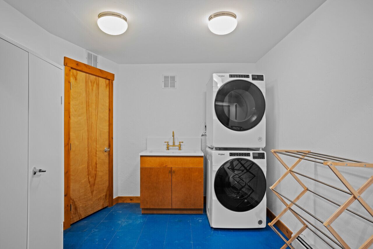 A laundry room with two stacked washing machines, a wooden cabinet, a sink, and a drying rack.