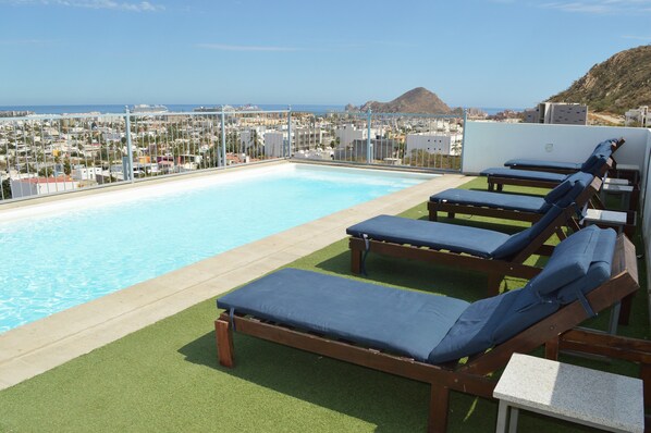 A rooftop pool with lounge chairs and a view of the city and mountains.