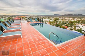 Una piscina infinita en la azotea con vistas a un paisaje urbano y montañas.