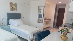 Habitación de hotel con cama, mesita de noche, silla, escritorio y baño visible a través de una puerta abierta.