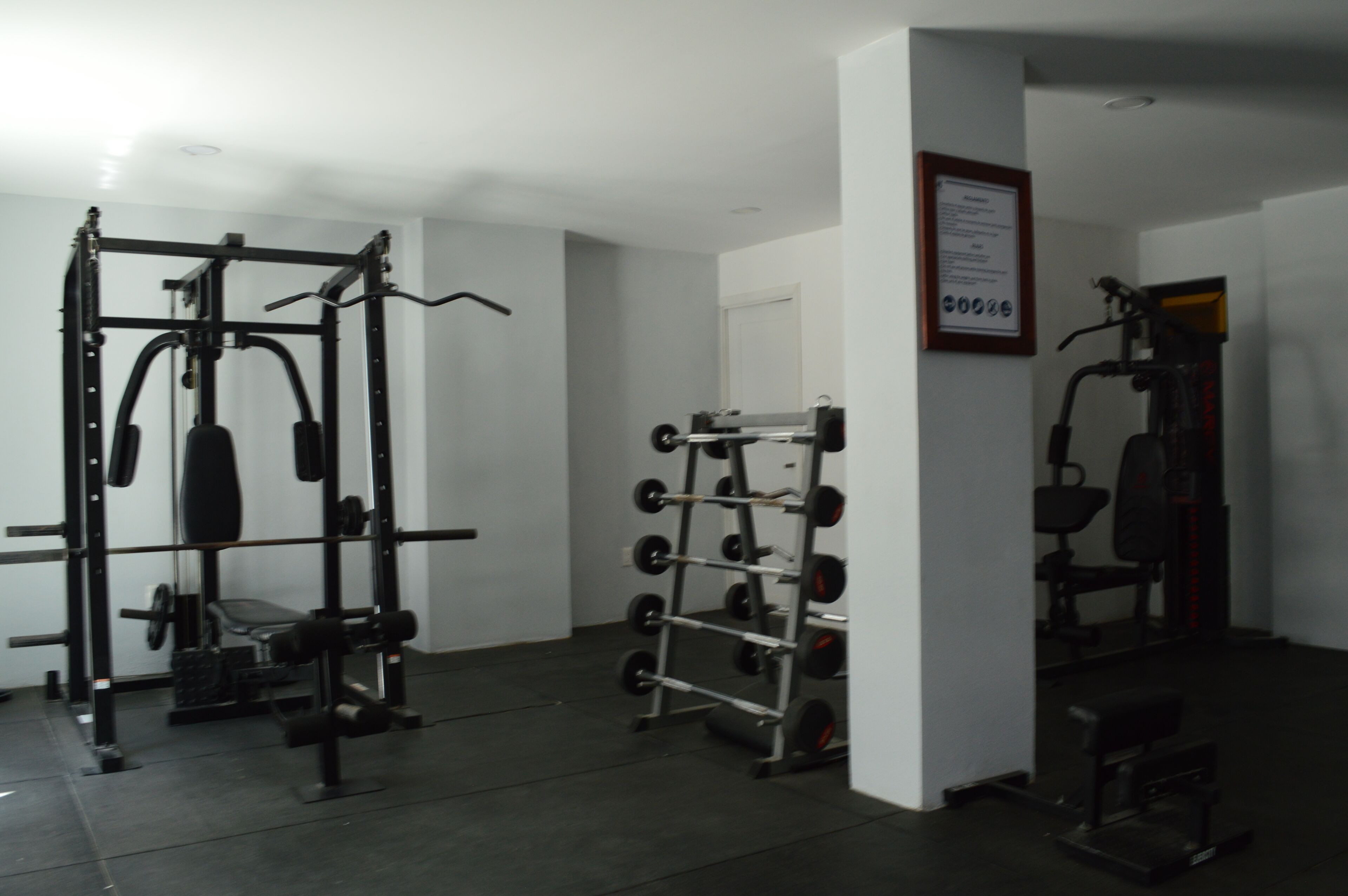 Un gimnasio con equipo de levantamiento de pesas, una estructura para sentadillas y una banca.