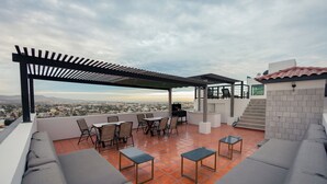 Una terraza en la azotea con mobiliario exterior, una pérgola y vistas de la ciudad.