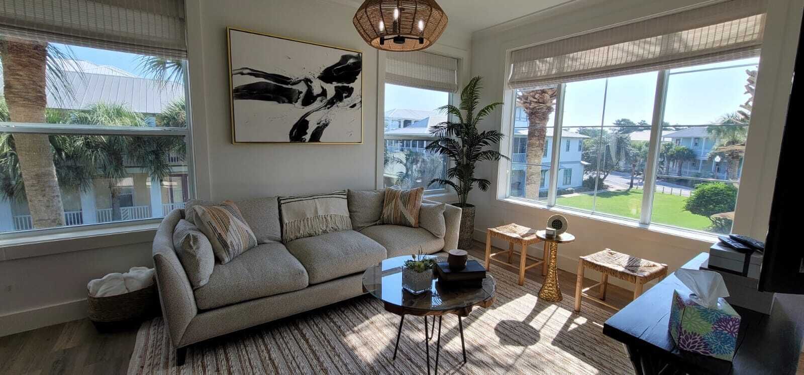 A living room with a sofa, a coffee table, and a large window with a view of a residential area.