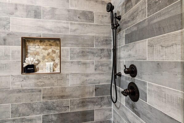 A shower area with a wooden-textured wall, a framed decorative item, and a handheld showerhead. - Hidden Cove Chalet 5 Bedroom Cabin by RedAwning (Sevierville)