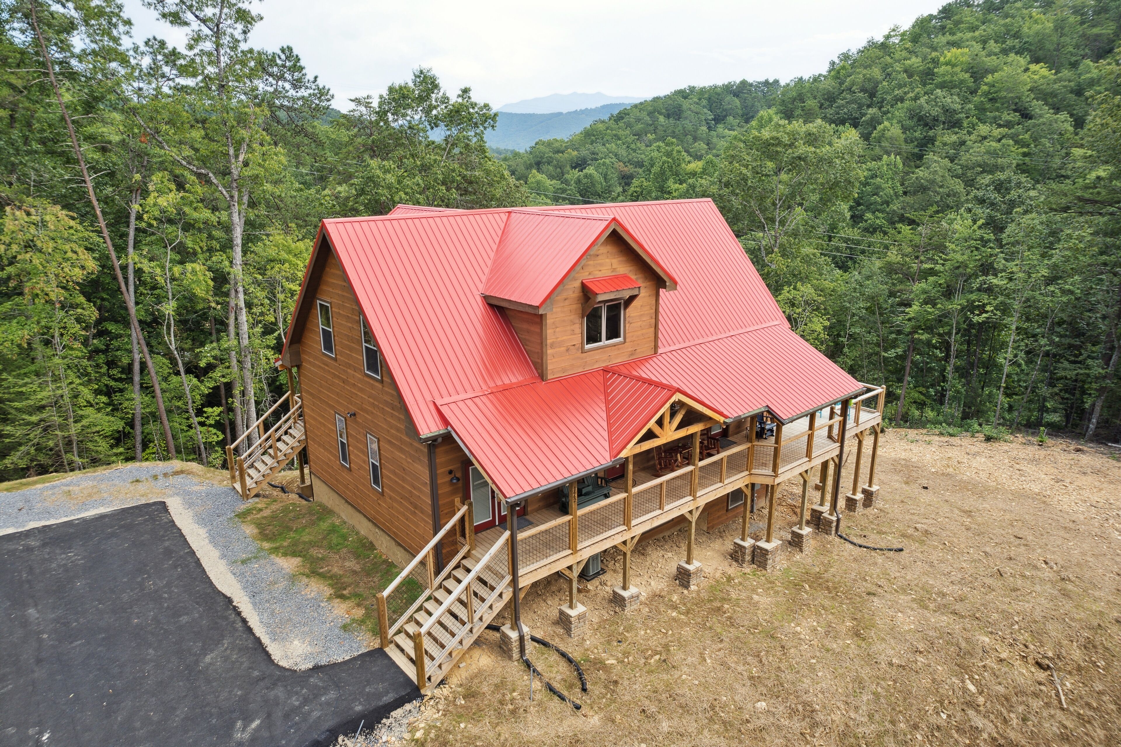 A cabin with a red roof, wooden deck, and a view of a forested area.
