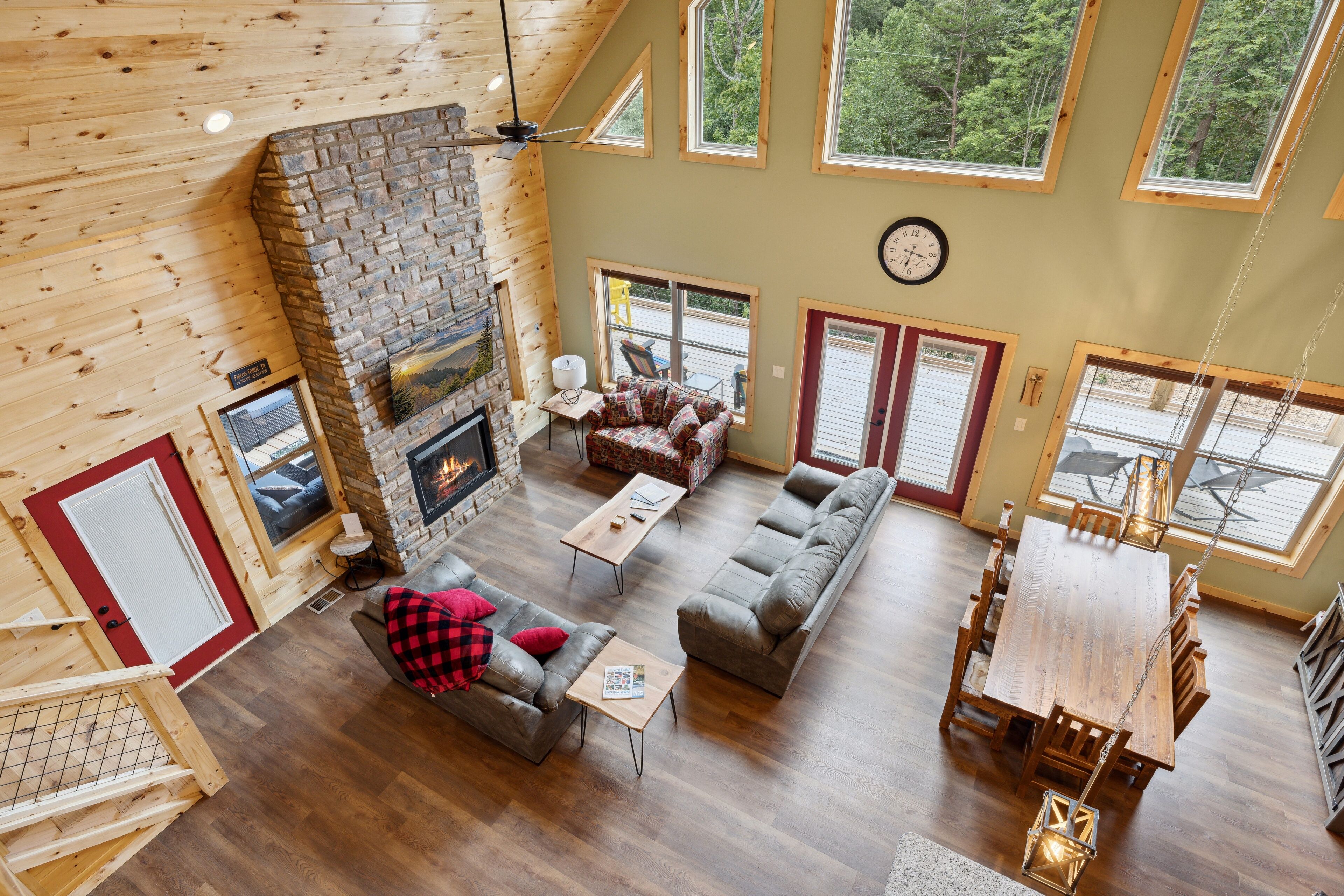 A spacious living area with a stone fireplace, wooden floors, and large windows offering a view of the outdoors.