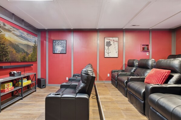 A room with red walls, black leather sofas, a wooden floor, and a bookshelf with books and a speaker. - Hidden Cove Chalet 5 Bedroom Cabin by RedAwning (Sevierville)