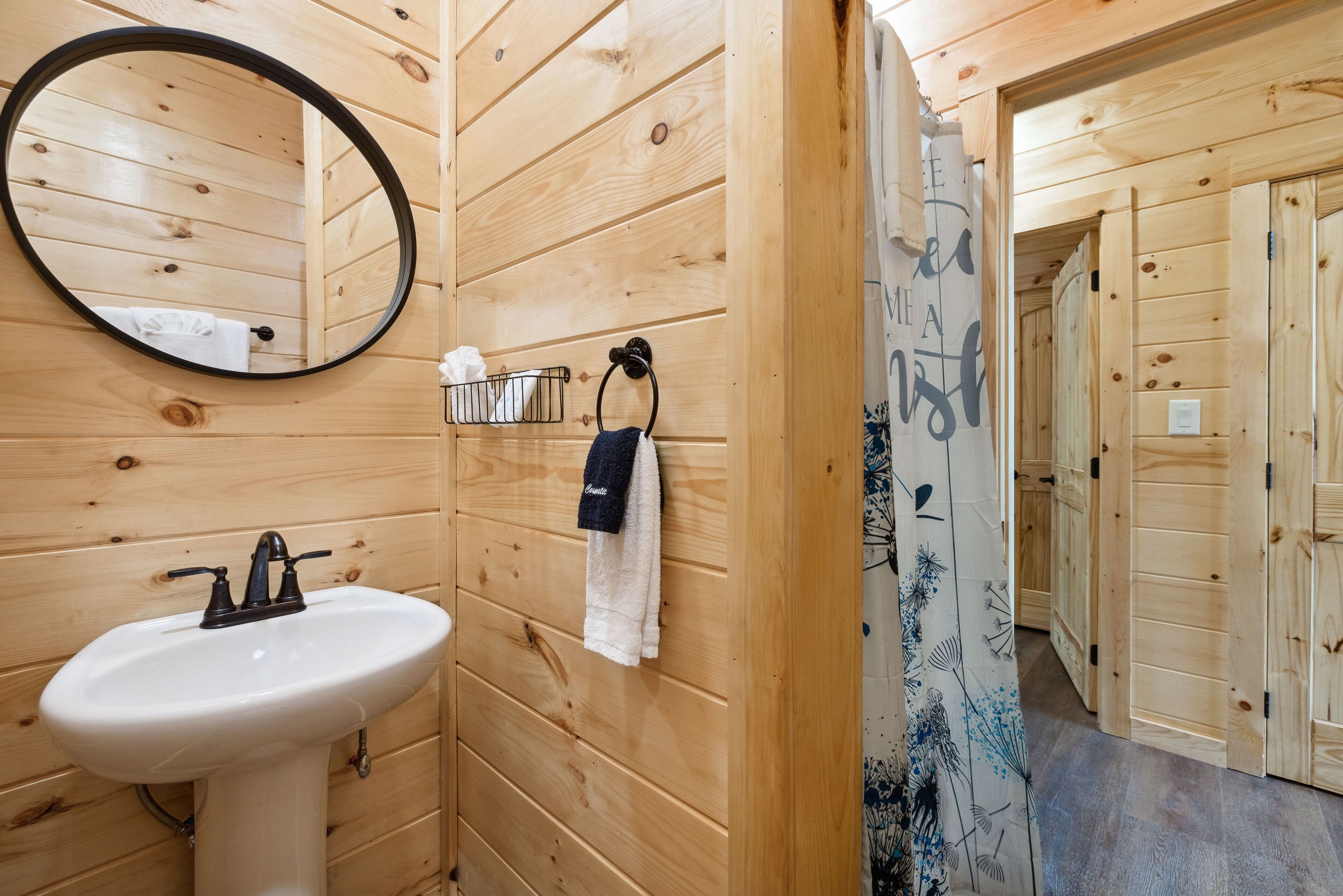 A wooden bathroom with a white sink, a round mirror, and a towel rack.