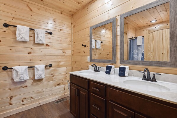 A wooden-paneled bathroom with a double sink, two towel racks, and a large mirror. - Hidden Cove Chalet 5 Bedroom Cabin by RedAwning (Sevierville)