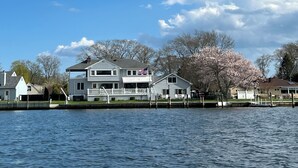 A waterfront property with a two-story house, dock, and a tree with pink blossoms. - Waterfront home, deck, bbq, fire pit, boats, hot tub, and more!  (Oakdale)