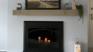 A fireplace with a framed painting above it, a small shelf with decorative items, and a wall-mounted vent. - Waterfront home, deck, bbq, fire pit, boats, hot tub, and more!  (Oakdale)