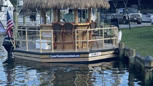 Un bote con zona de bar con techo de paja, sillas de madera y una pequeña mesa.