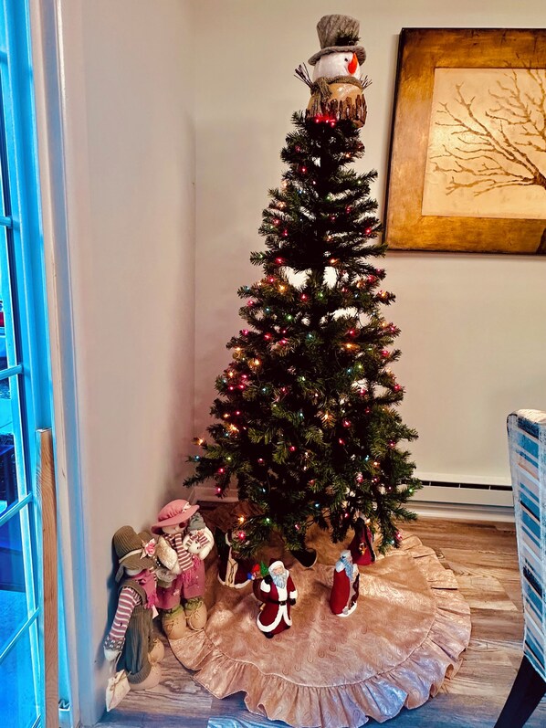Un árbol de Navidad con luces y adornos, un osito de peluche y una figura de Papá Noel sobre una falda rosa.