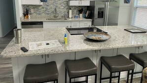 Cocina moderna con armarios blancos, encimeras de granito, refrigerador de acero inoxidable y una isla grande con taburetes de bar.