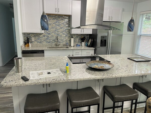 Cocina moderna con armarios blancos, encimeras de granito, refrigerador de acero inoxidable y una isla grande con taburetes de bar.