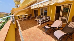 A balcony with a sofa, chairs, and a table, overlooking a swimming pool.