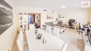 A modern living room with a white sofa, a dining table, and a workspace with a desk and computer.