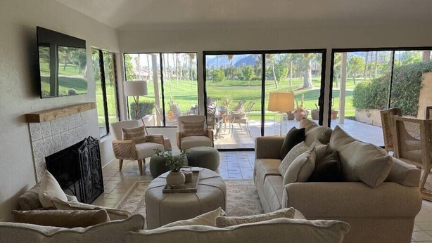 Ein geräumiges Wohnzimmer mit Kamin, bequemen Sitzmöglichkeiten und großen Fenstern mit Blick auf einen Golfplatz.