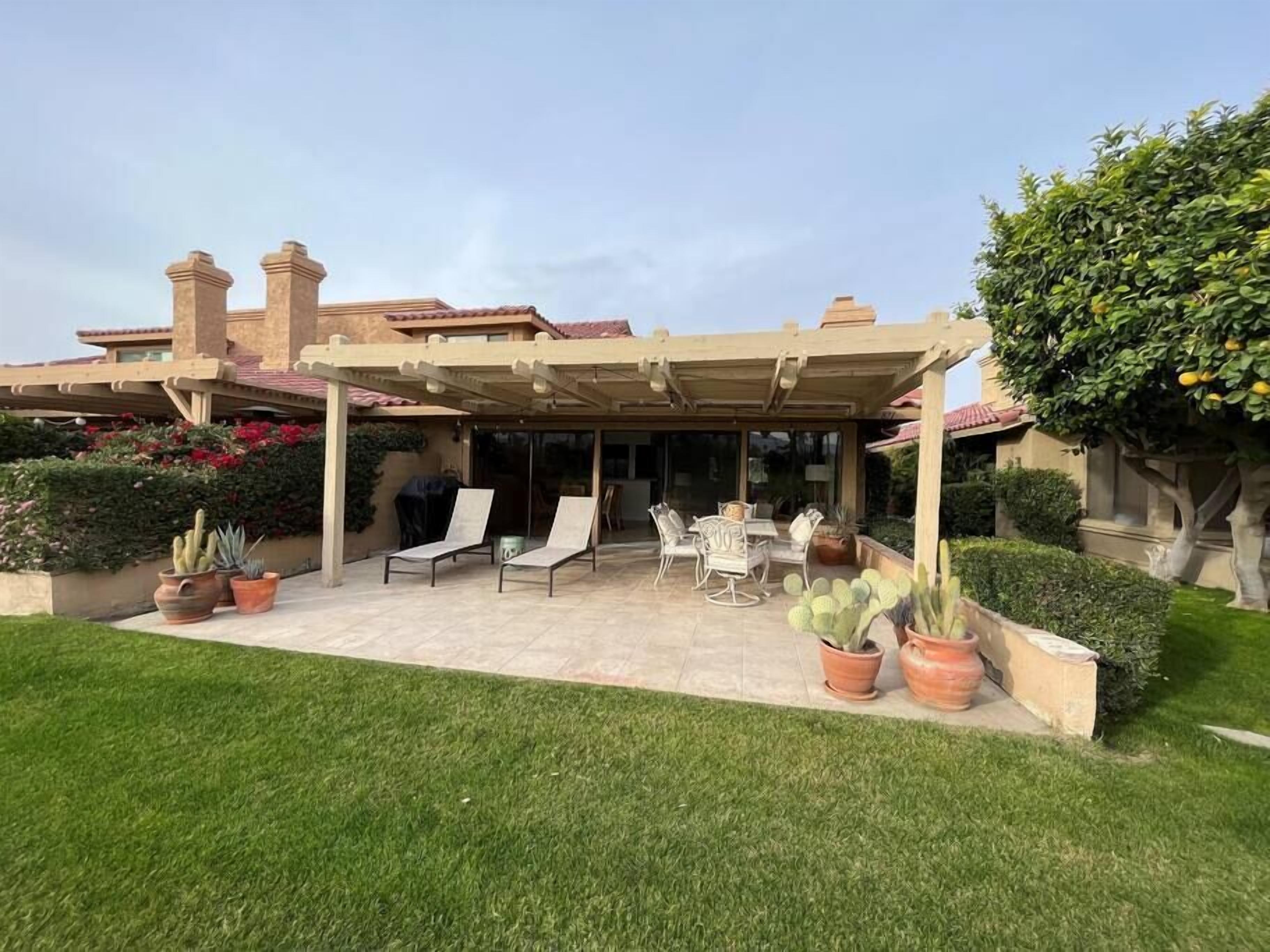 Une terrasse couverte, aménagée avec du mobilier d’extérieur, une pergola et des plantes en pot.