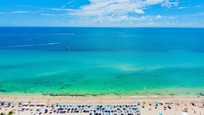 A beach with clear turquoise waters, a sandy shore, and numerous umbrellas. - HYDE 3BR OceanFront Suite w SunriseTo Sunset Views (Hollywood)
