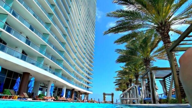 A swimming pool with clear blue water, surrounded by palm trees and a modern hotel building with balconies. - HYDE 3BR OceanFront Suite w SunriseTo Sunset Views (Hollywood)