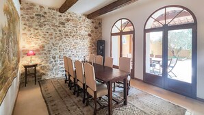 Ein Essbereich mit einer Steinwand, einem Holztisch mit acht Stühlen, einem gemusterten Teppich und großen Bogenfenstern.