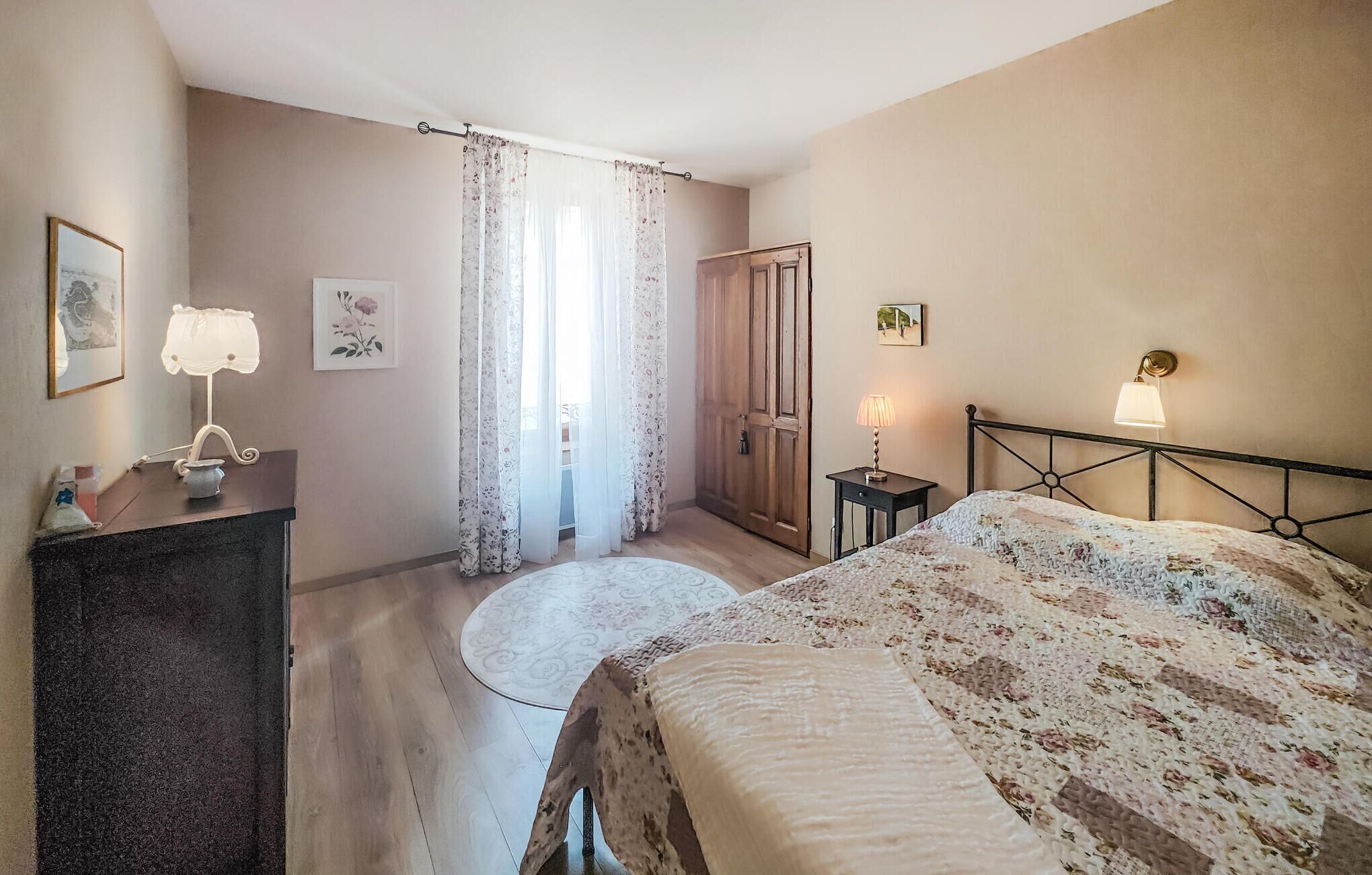 A bedroom with a bed, a desk, a chair, a door, and a window with curtains.