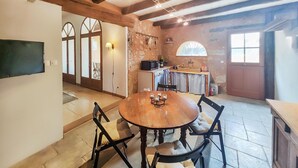 Ein gemütlicher Essbereich mit Holztisch und -stühlen, eine Küche im Hintergrund und eine Steinwand.