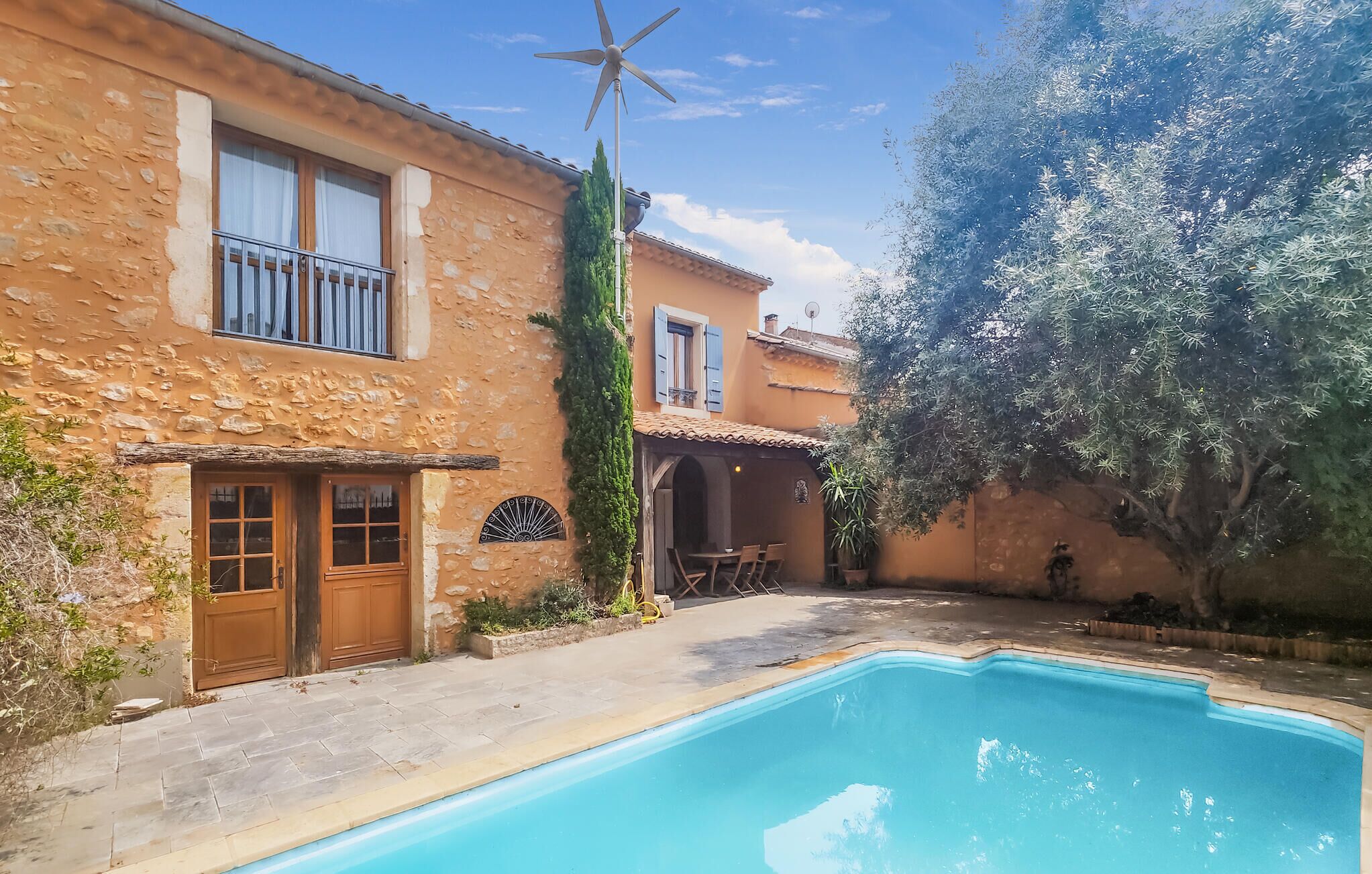 A stone building with a swimming pool, a wind turbine, and a tree.