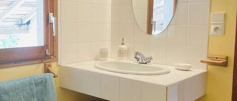 Une salle de bain avec un lavabo blanc, un miroir et deux paniers en osier posés sur une étagère en bois.