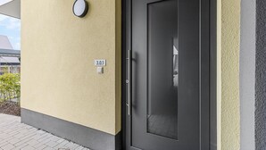 Entrada de un edificio moderno con una puerta oscura, un reloj redondo pequeño y una placa con el número 3.0.1.