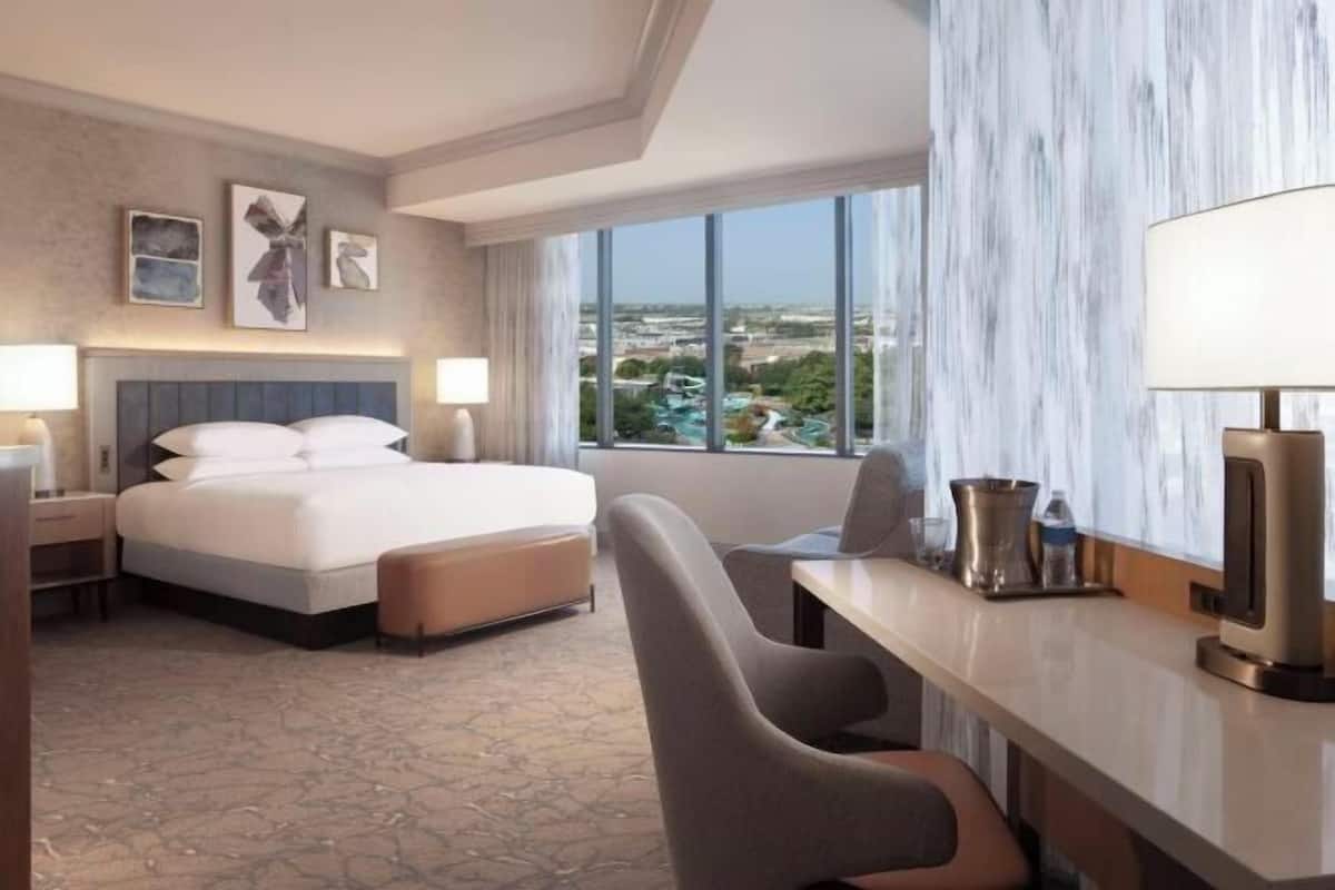 Une chambre d’hôtel équipée d’un lit, d’un bureau, d’une chaise, d’une lampe et offrant une vue sur le paysage urbain.